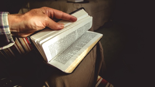 A man holding a Bible on its lap flipping through pages.