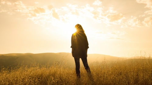 A woman standing in front of sun rays in an open field.