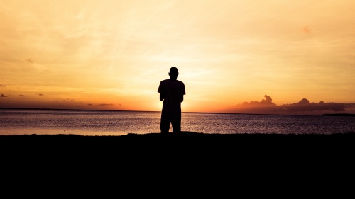 A person standing by a body of water at sunset.