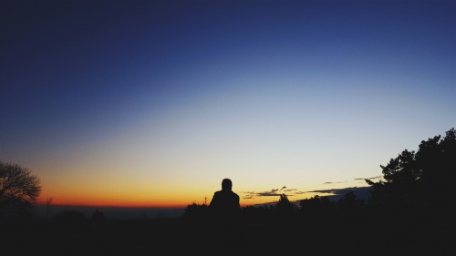 A person sitting at the top of hill looking at the expanse of the night sky.
