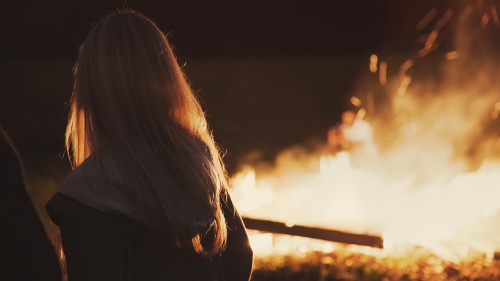 A woman standing by a bonfire.