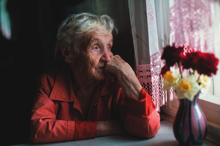 An older women sitting by a window looking outside.