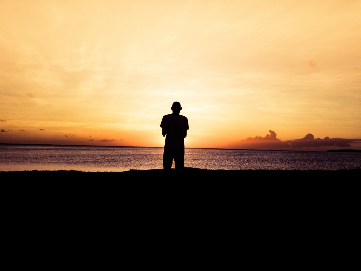 A person standing by a body of water at sunset.