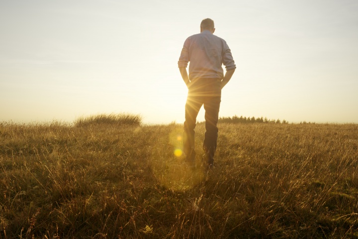 Photo of a man walking in a field toward the sun at golden hour.